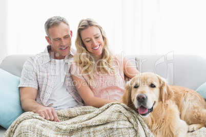 Affectionate couple sitting on sofa under blanket with their dog