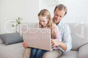 Casual father and daughter using laptop on the couch