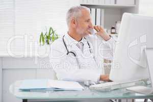 Smiling doctor phoning and using computer
