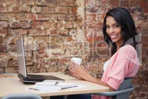 Smiling woman drinking coffee at her desk using laptop