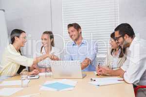 Casual business people shaking hands at desk and smiling