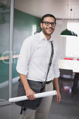 Casual architect smiling at camera holding blueprint