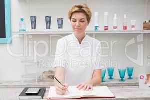 Pretty beautician writing in appointment book