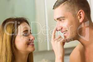 Cute woman putting cream on boyfriends nose