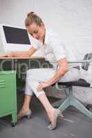Businesswoman suffering from leg pain at office desk