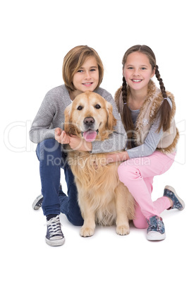 Smiling siblings petting their golden retriever