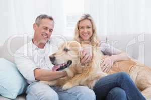 Smiling couple petting their golden retriever on the couch