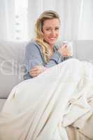 Woman holding a cup sitting on couch under a blanket