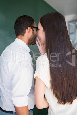 Businesswoman whispering into male colleagues ear