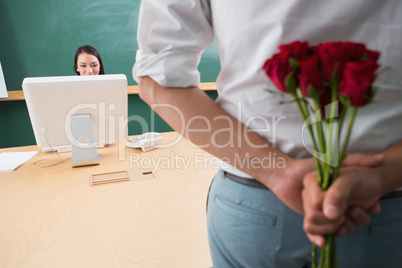 Man hiding bouquet in front of businesswoman at desk