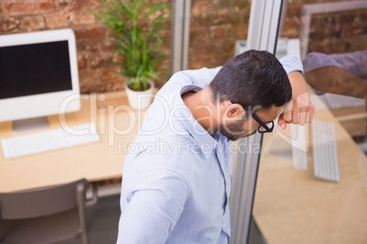 Thoughtful businessman standing against glass wall at office