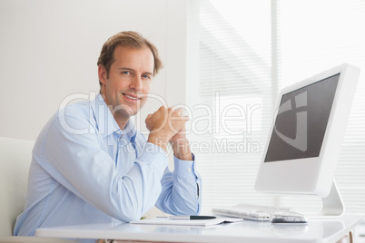 Casual businessman smiling at camera at his desk