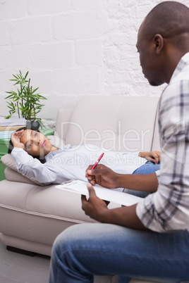 Worried woman lying on the couch while psychologist writing