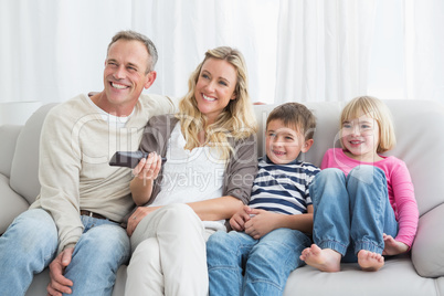 Smiling family sitting on sofa changing tv channel