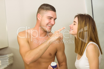 Handsome man putting cream on girlfriends nose