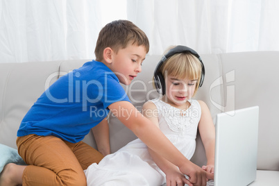 Siblings using a headphone and a tablet sitting on a couch