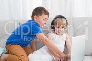 Siblings using a headphone and a tablet sitting on a couch