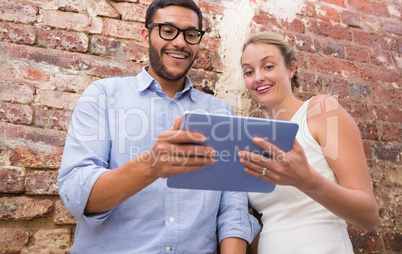 Colleagues using digital tablet against brick wall