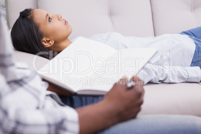 Woman lying on the couch while psychologist writing
