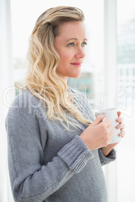 Smiling blonde woman holding mug of coffee looking away