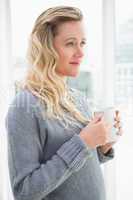 Smiling blonde woman holding mug of coffee looking away