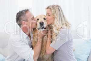 Smiling couple kissing their golden retriever on the couch
