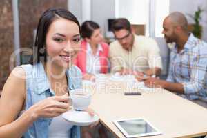 Woman drinking a coffee while his colleague work behind her
