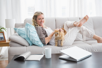 Cheerful woman lying on sofa cuddling a ginger cat