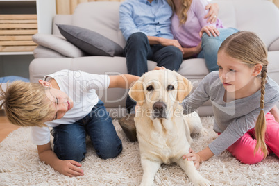 Parents watching children on rug with labrador