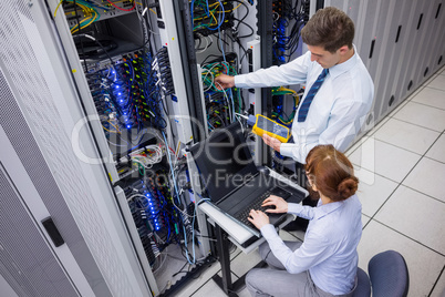 Team of technicians using digital cable analyser on servers