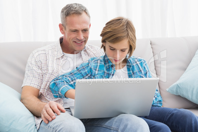 Father with son sitting on the couch using laptop Father with son sitting on the couch using laptop