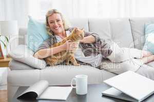 Cheerful woman lying on sofa cuddling a ginger cat