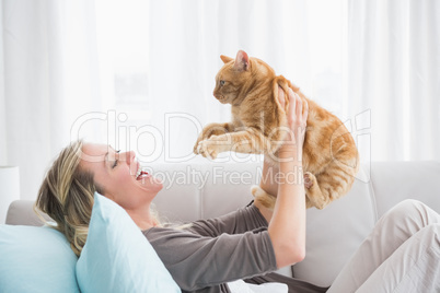 Cheerful woman lying on sofa holding a gringer cat