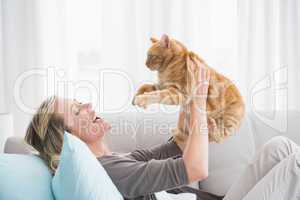 Cheerful woman lying on sofa holding a gringer cat
