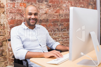 Worker in wheelchair working on computer smiles to camera