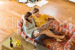 Young couple cuddling on the couch with laptop