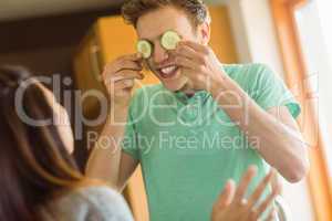 Cute man holding cucumber slices over eyes