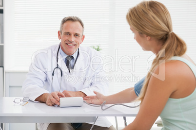 Smiling doctor taking patients blood pressure