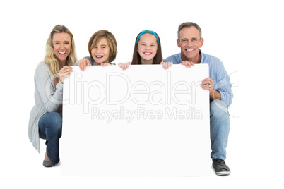 Cute family smiling at camera holding poster