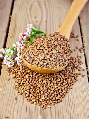 Buckwheat in wooden spoon with flower on board