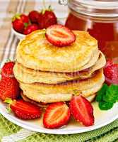 Flapjacks with strawberries and honey on tablecloth