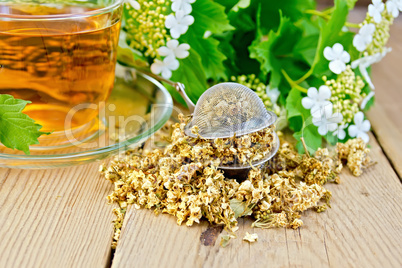 Tea from flowers of viburnum in glass cup and strainer on board