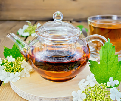 Tea from flowers of viburnum in glass teapot on board