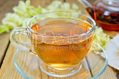 Tea from meadowsweet in glass cup and teapot on board