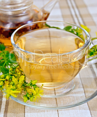 Tea from tutsan in glass cup and teapot on tablecloth