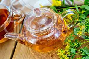 Herbal tea from tutsan in glass teapot with cup on board