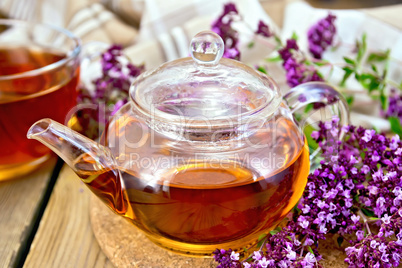 Tea of oregano in glass teapot on board with napkin