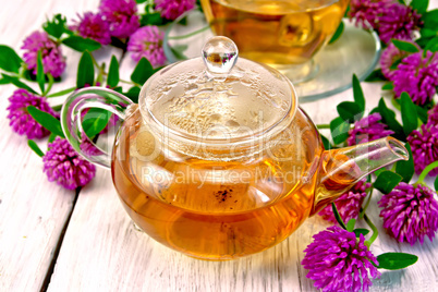 Tea with clover in glass teapot on light board