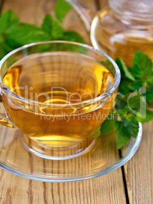 Tea with mint in cup and teapot on wooden board