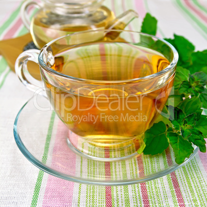 Tea with mint in cup and teapot on tablecloth